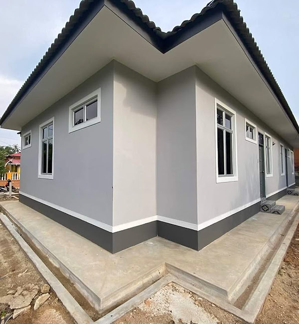 Long grey bungalow elevation with concrete apron and drain