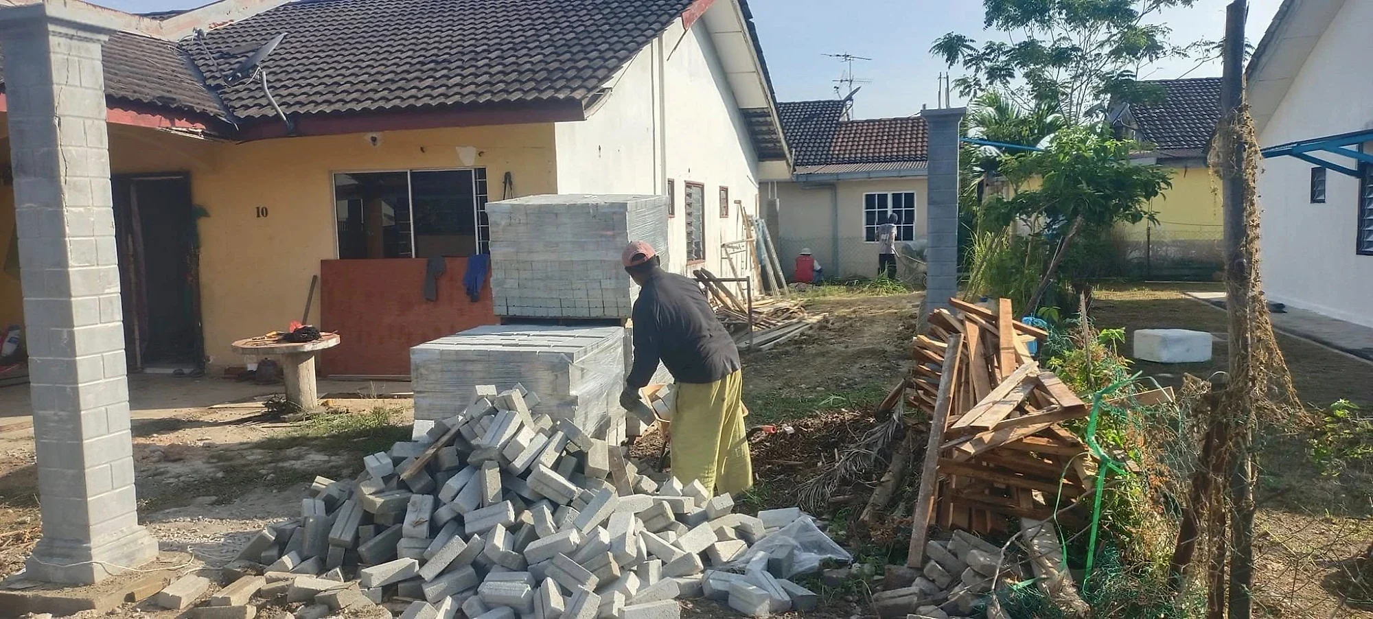 Worker stacking bricks beside the house, with timber and new columns
