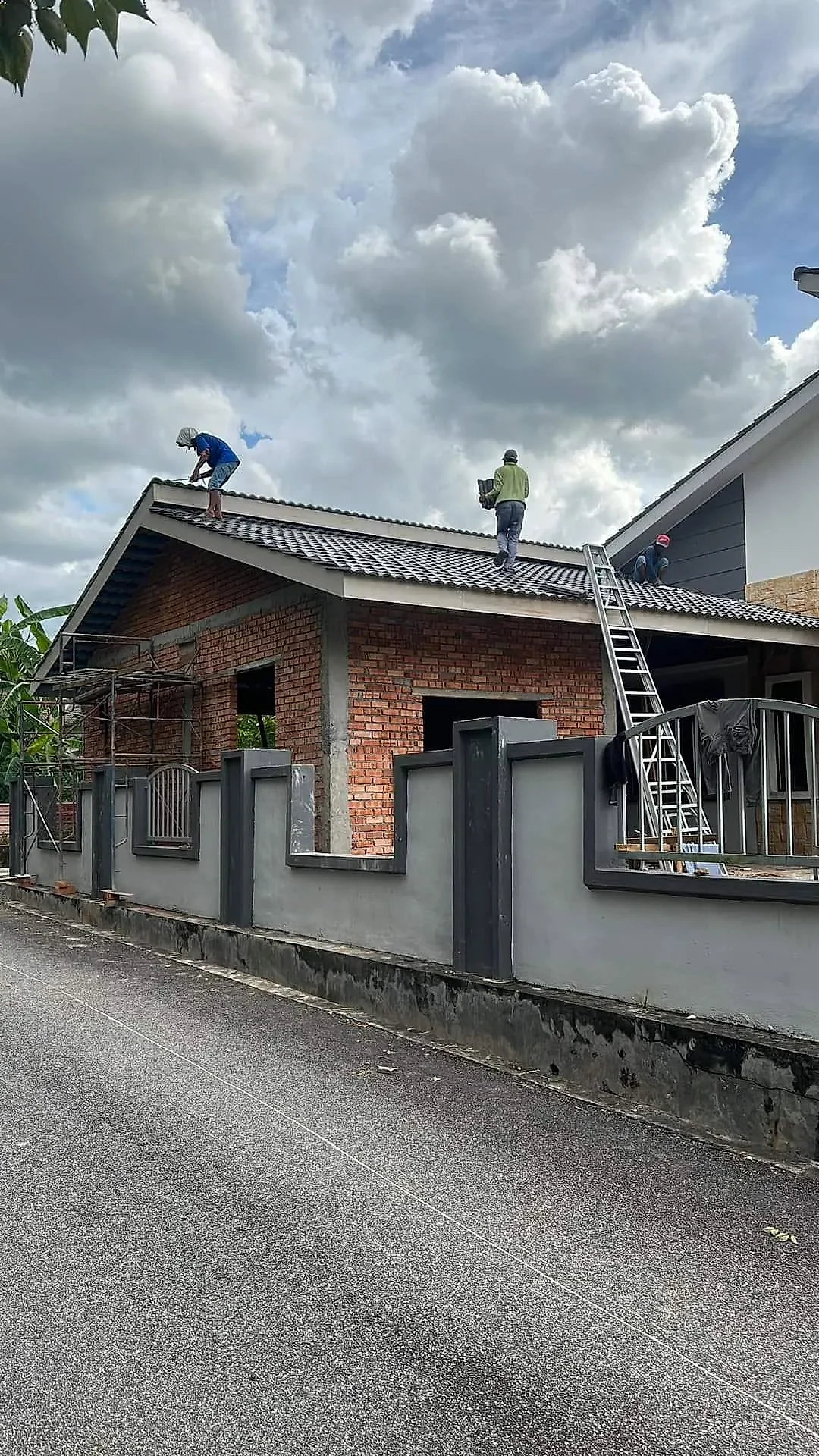 Roofers tiling the extension roof, seen from the road over the front fence