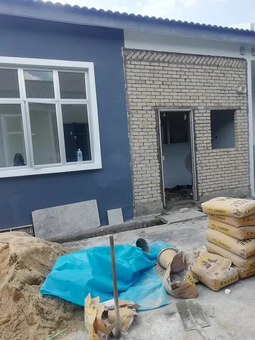 Brick extension with door and window openings beside a painted house