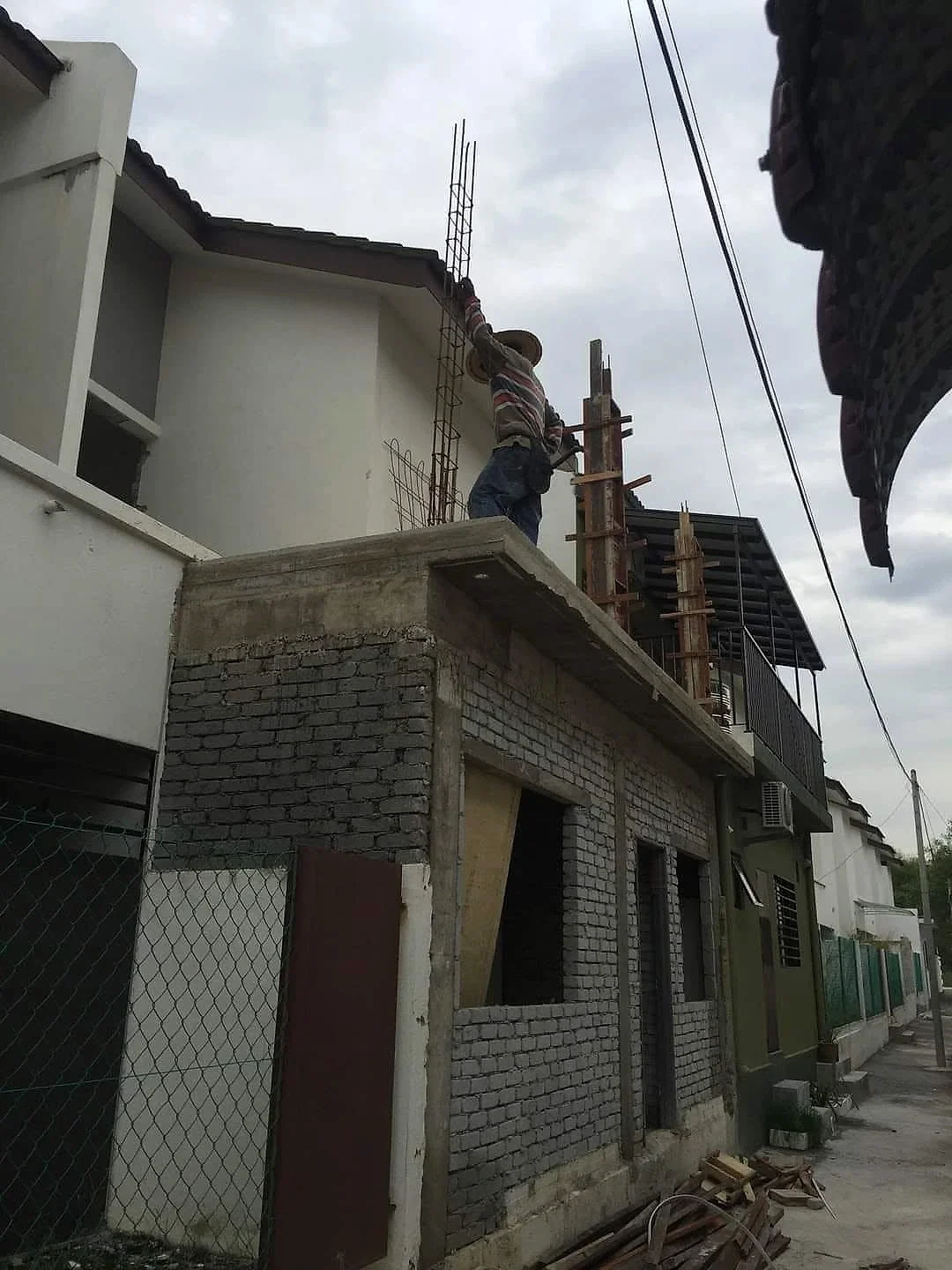 Worker fixing steel bars and formwork for upper-floor columns on top of the brick extension