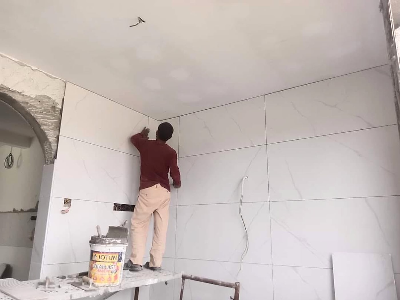 Tiler fixing large white marble-look tiles up to the ceiling