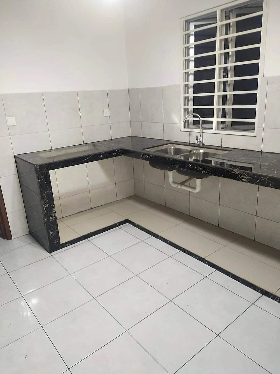 Finished kitchen with a black marble-look L-shaped counter, double sink and white floor tiles