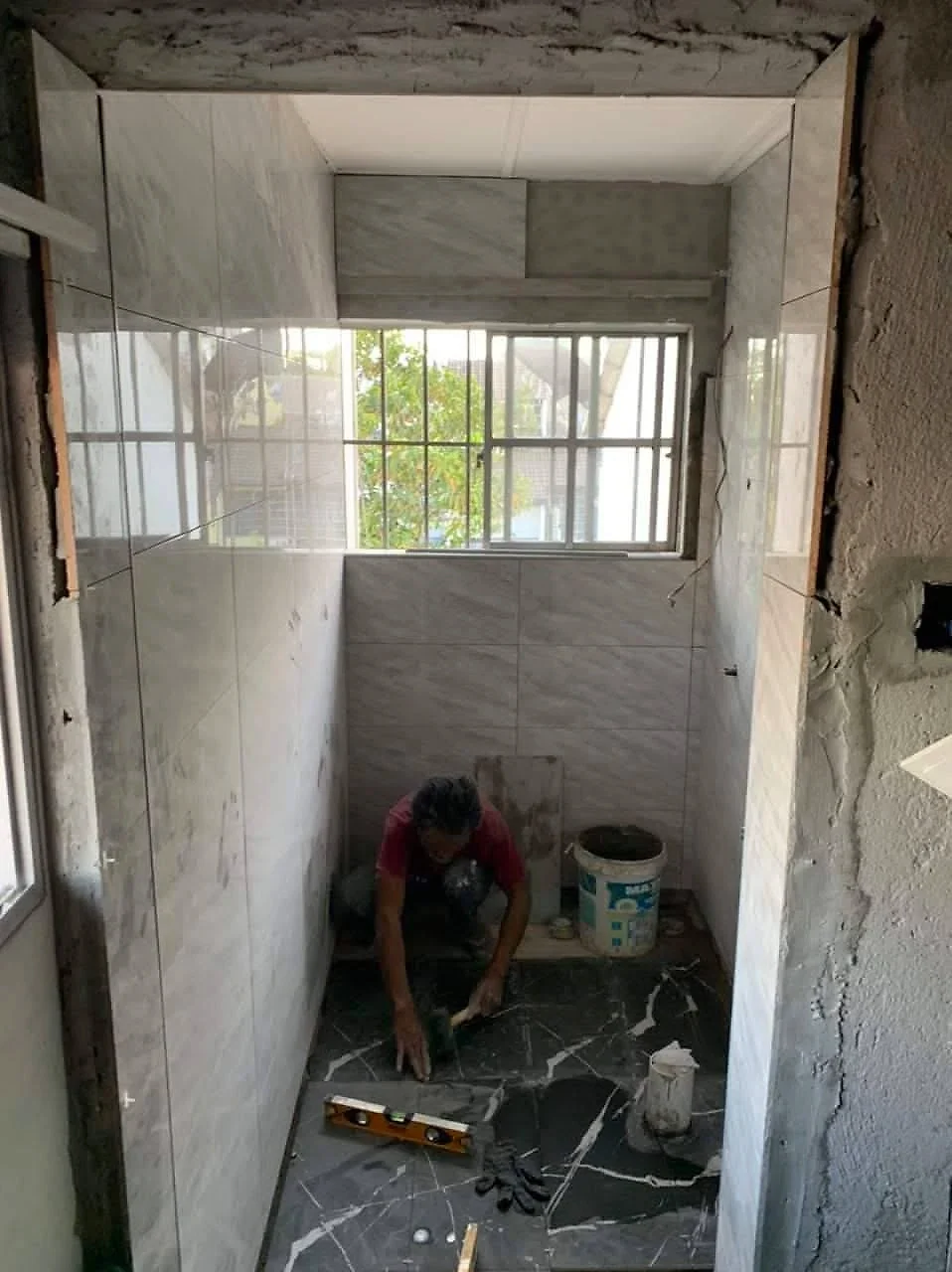 Tiler laying a black marble-look floor in a bathroom with grey wall tiles