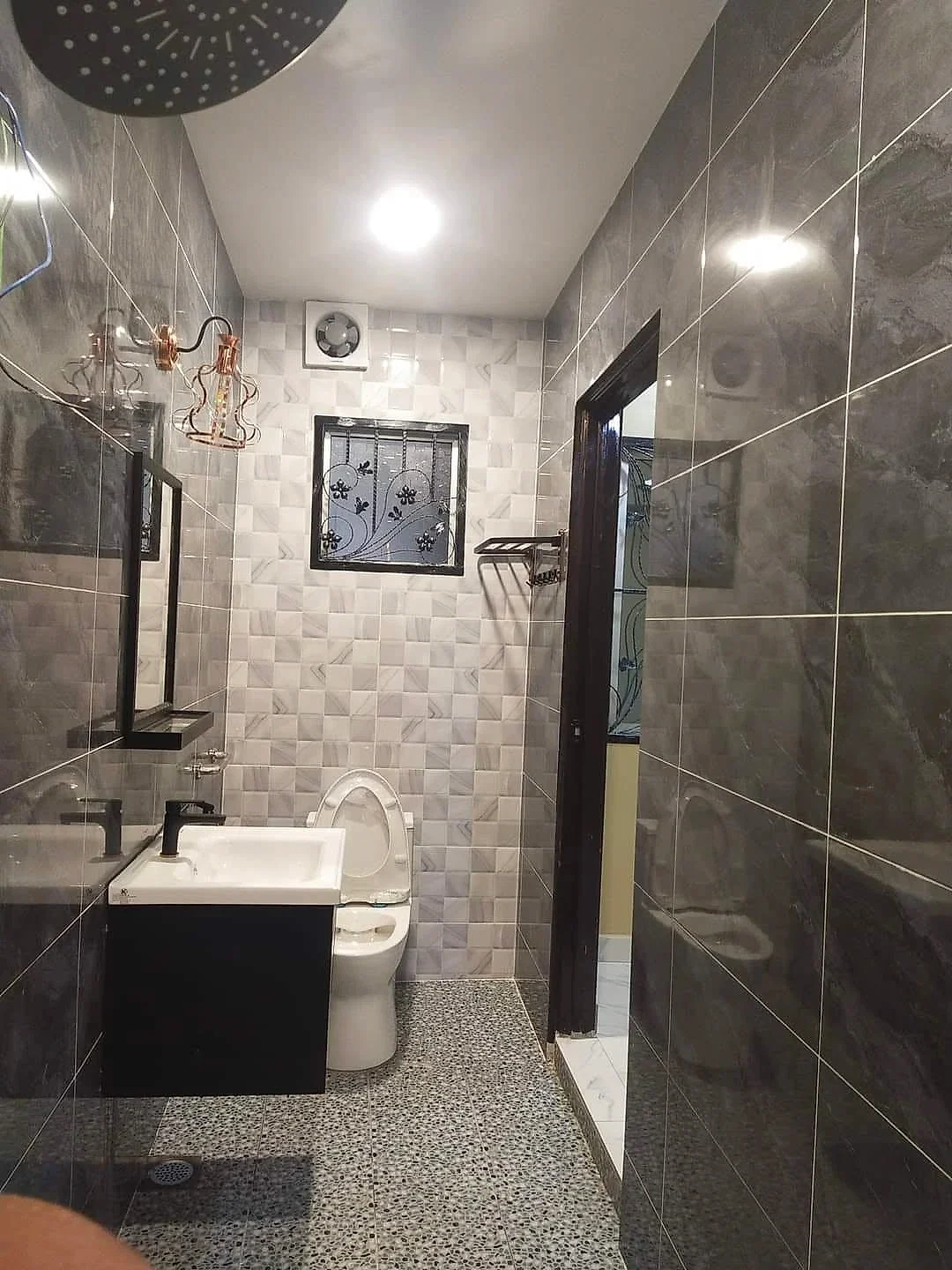 Finished bathroom with dark grey stone-look tiles, pebble-look floor, black vanity and rain shower