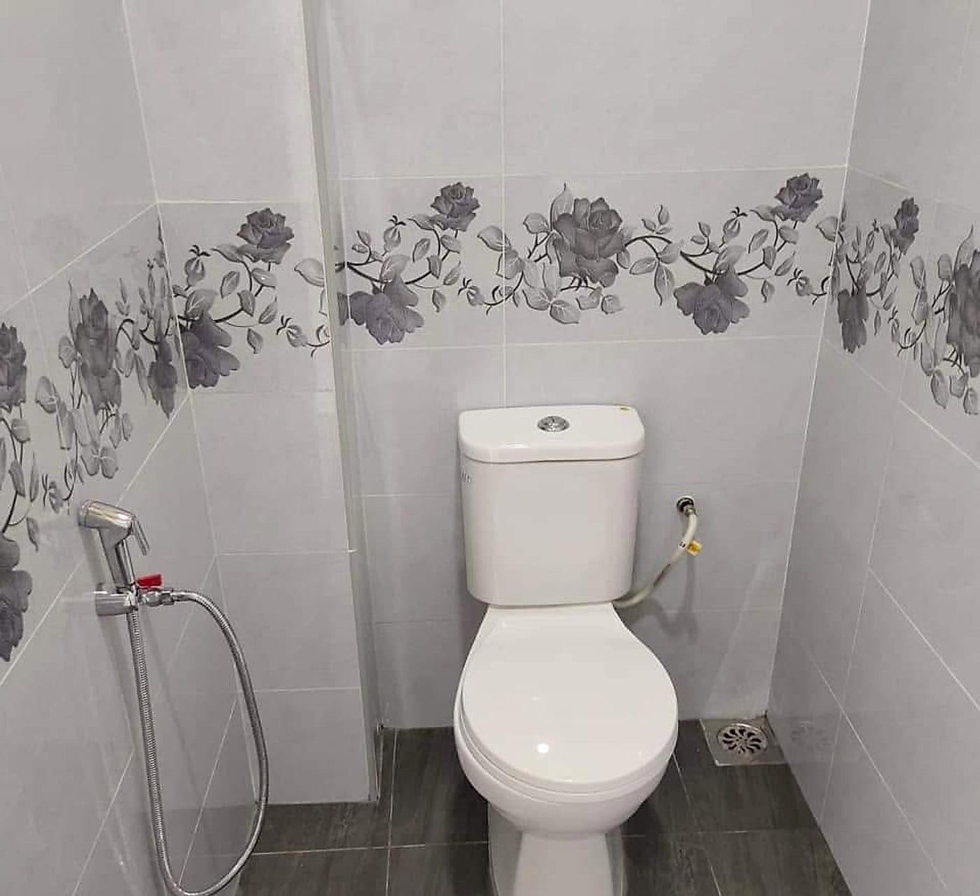 New toilet and bidet spray against light grey tiles with a floral border