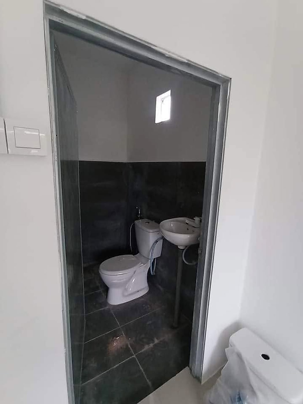 Finished toilet with dark wall and floor tiles, toilet and basin
