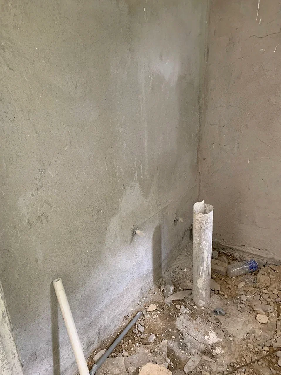 Plastered bathroom wall with pipe outlets and floor drain