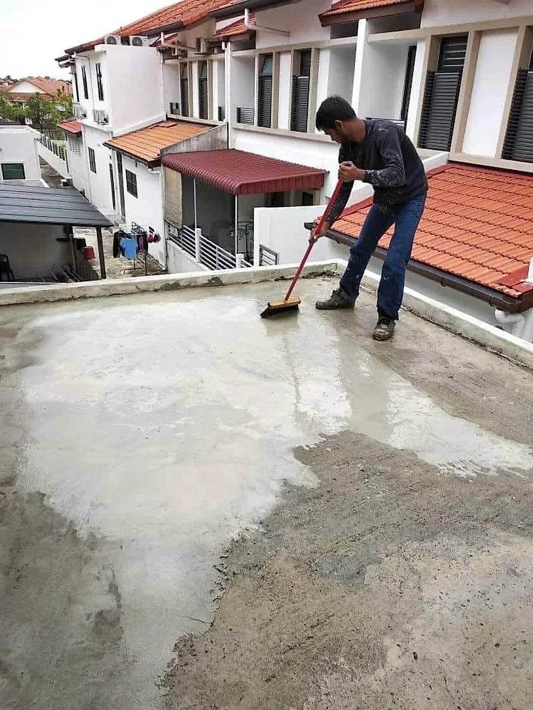 Worker brushing a cement slurry primer over a flat concrete roof