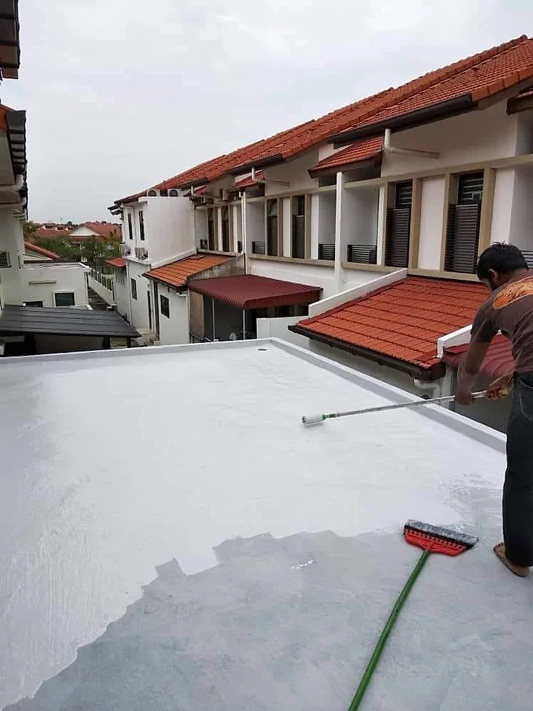 Worker rolling a white waterproof coat over the primed flat roof
