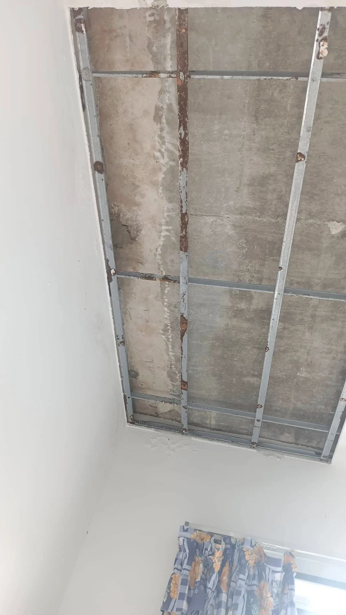 Ceiling opened to show water stains and rusted frame under the leaking slab
